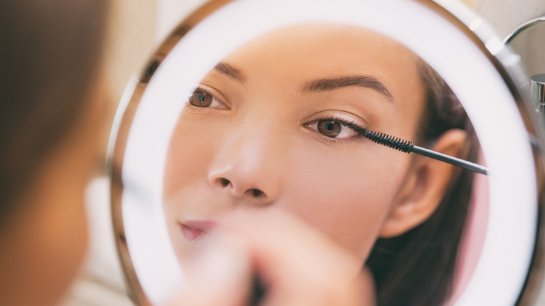 Woman doing eye makeup in mirror