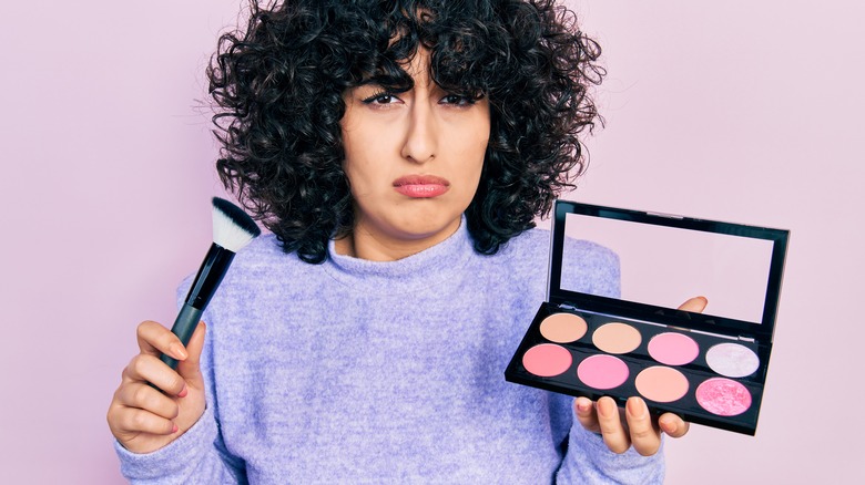 Frowning woman holding blush palette