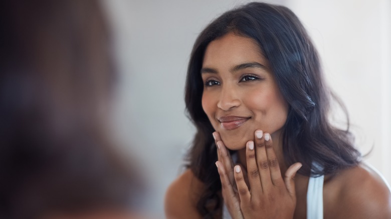 Woman happily inspects face in mirror