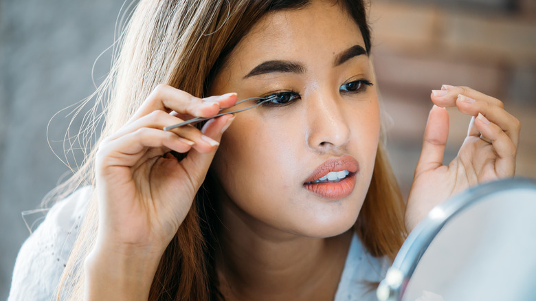 woman applying fake lashes with tweezers