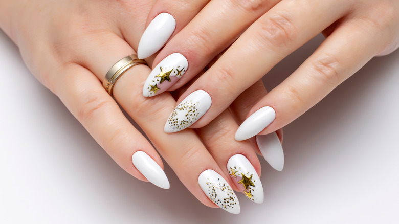 White, feminine hands with white nail polish and gold, starry accents