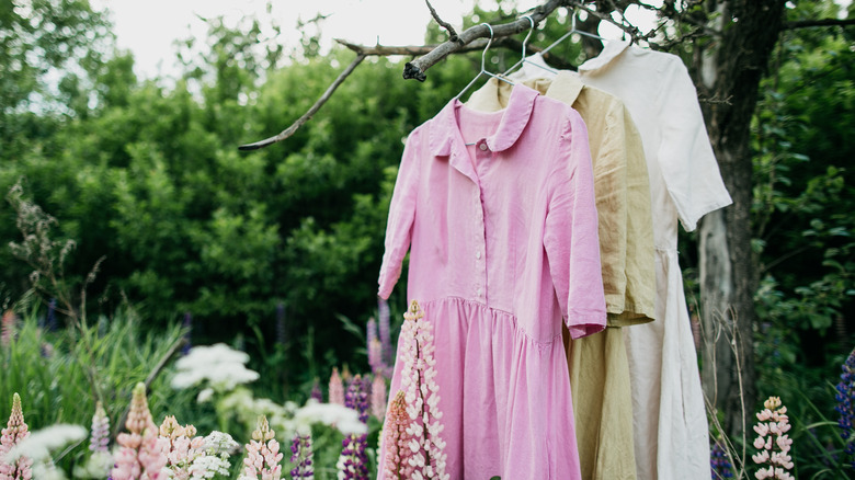 a pink, beige, and white linen dress are hung outdoors on a tree branch