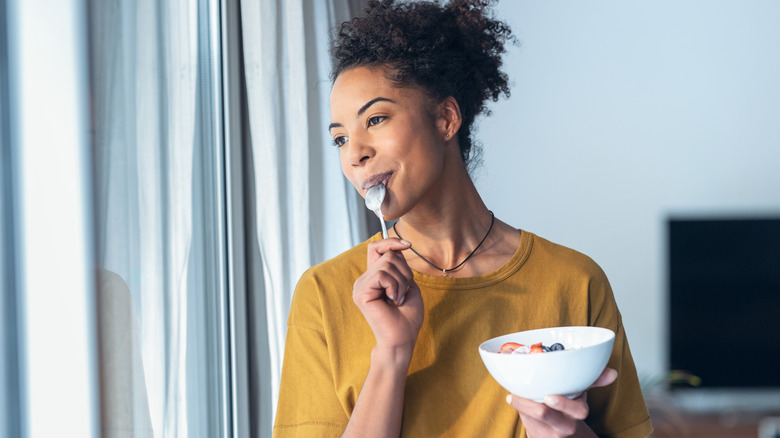 Woman eating from bowl, looking out window