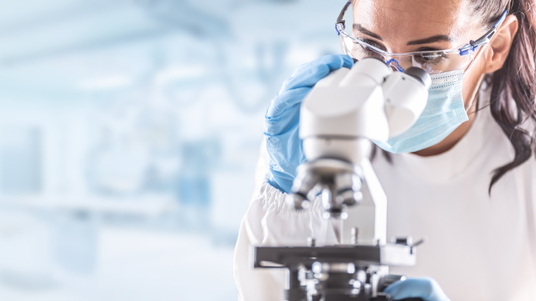 Woman in lab coat looks at microscope