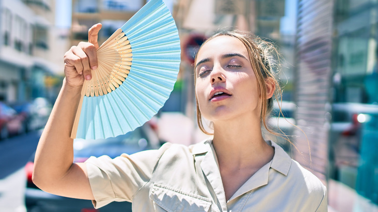 woman standing outside fans herself because it is hot