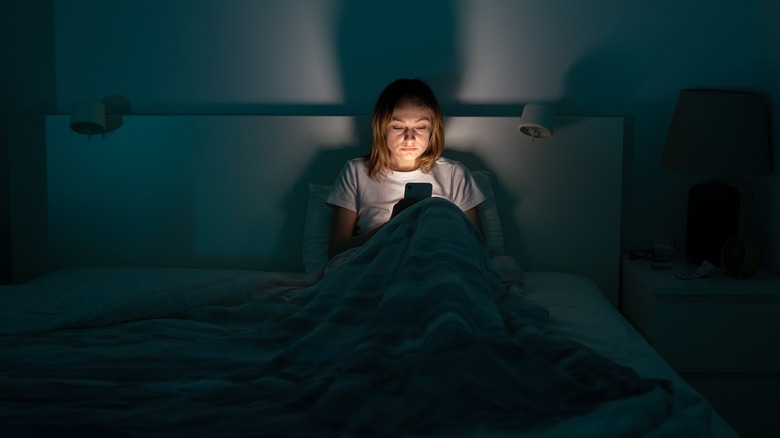 Woman scrolls social media in bed at night