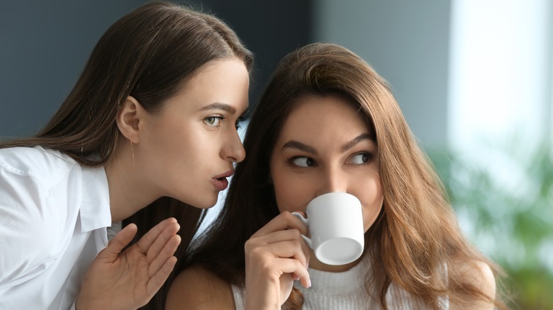 Woman whispering into another's ear