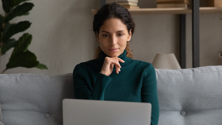 Woman sitting, reading laptop screen