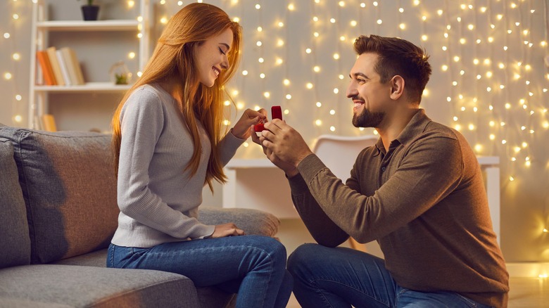 A man proposing to a woman at home in front of fairy lights