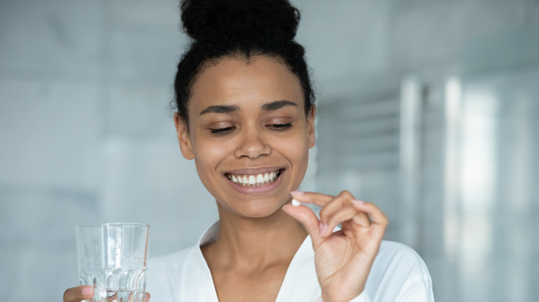 young woman holding glass of water and supplement