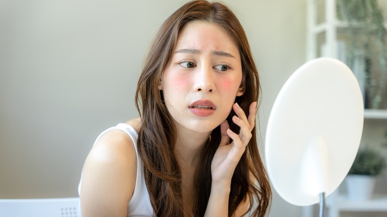 Woman with inflamed skin looking in the mirror