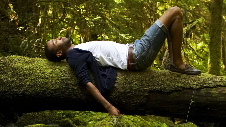 Man relaxing on fallen tree in forest