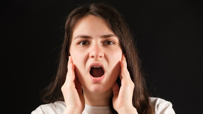 Woman touching jaw, mouth open