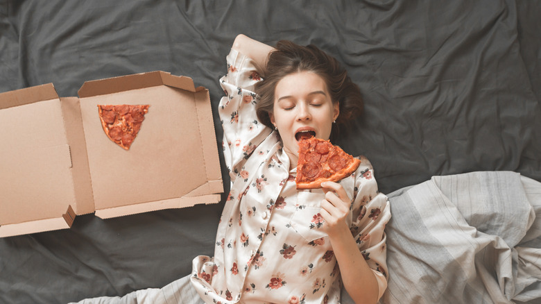 Woman eating pizza from box in bed