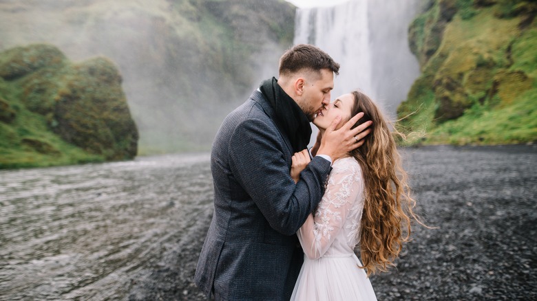 Bride and groom kiss before waterfall