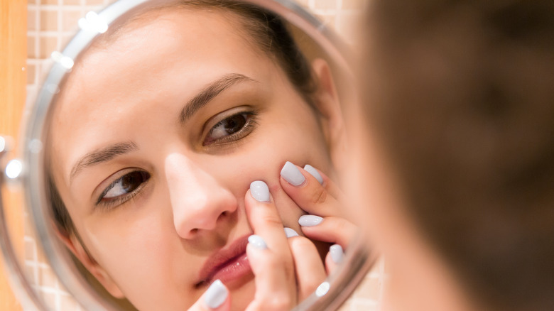 young woman picking at pimple in mirror