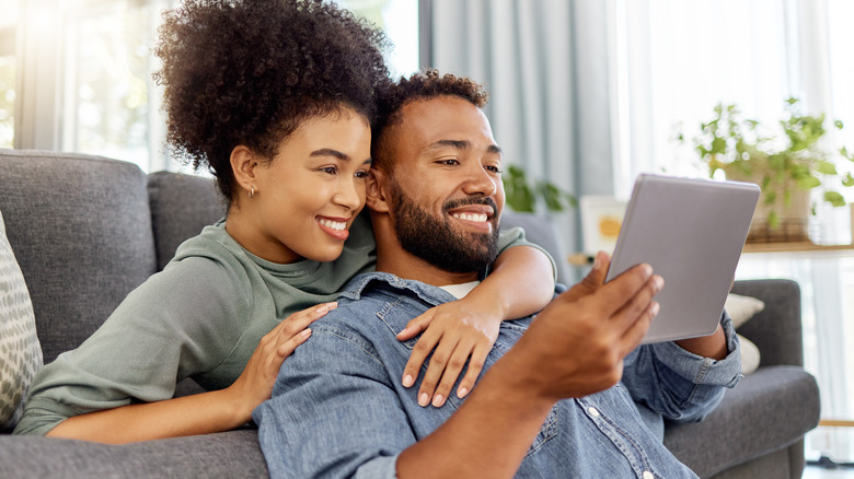 Couple embracing on sofa and watching tablet