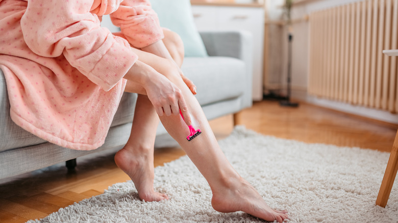 woman in bathrobe shaving legs