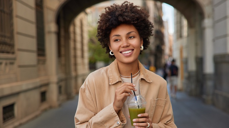 Woman sipping on green juice while walking down street