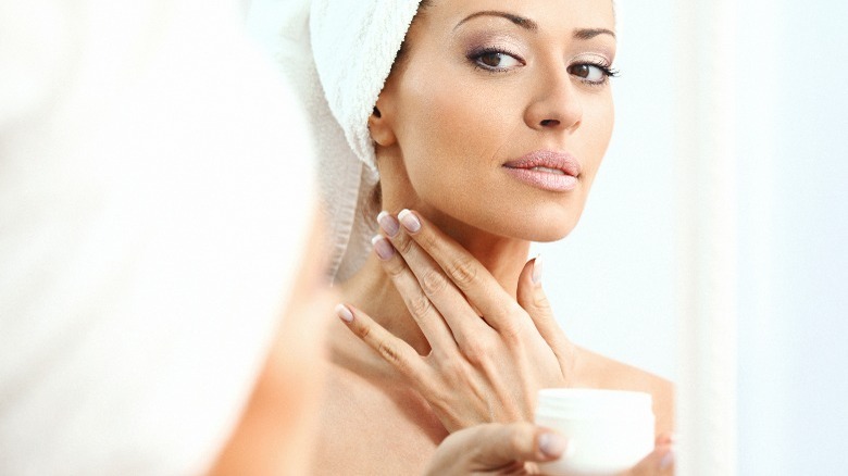 Woman applying neck cream in mirror