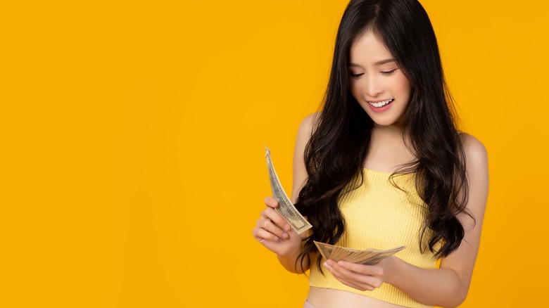 Woman counts money in front of yellow background