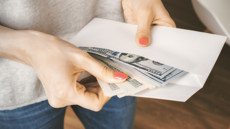 Woman with painted nails puts money in envelope