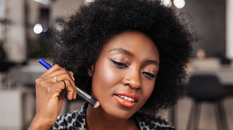 curly-haired woman applying concealer