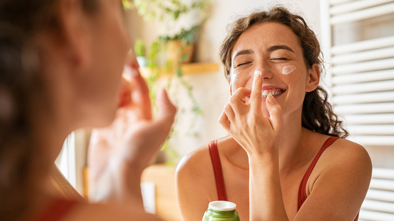 Woman moisturizing in mirror