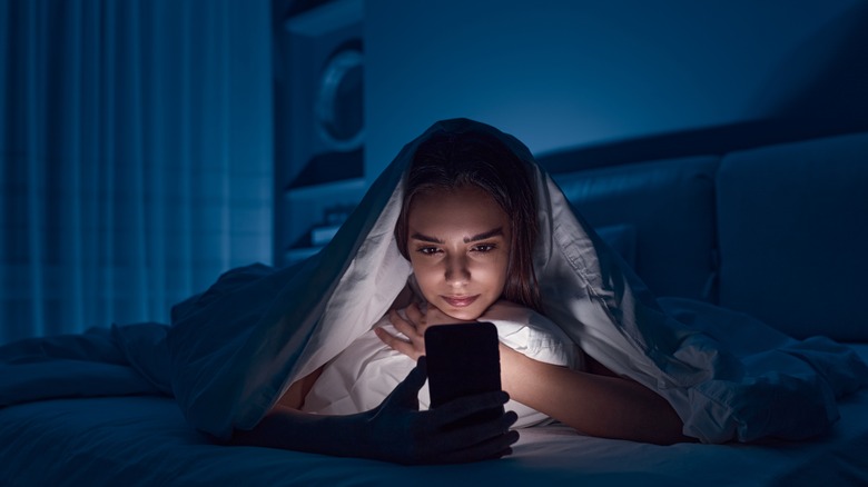 Woman watches cell phone in bed 