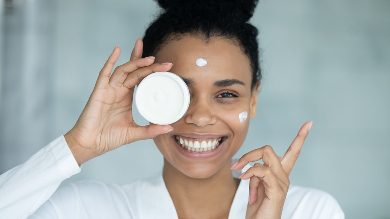 Smiling woman holding moisturizer by face