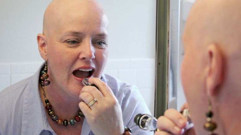 Bald mature woman applying lipstick