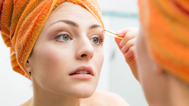 A woman plucking her eyebrows in the mirror.