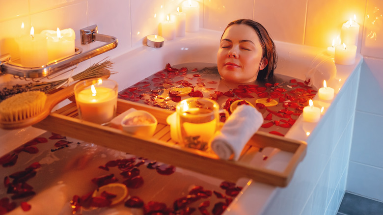 Woman bathes with flowers, fruits, and candles