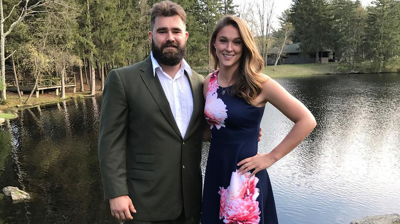 Jason and Kylie Kelce, in a floral dress, in front of a lake