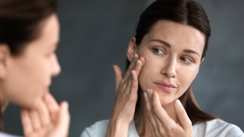 woman examining face in mirror