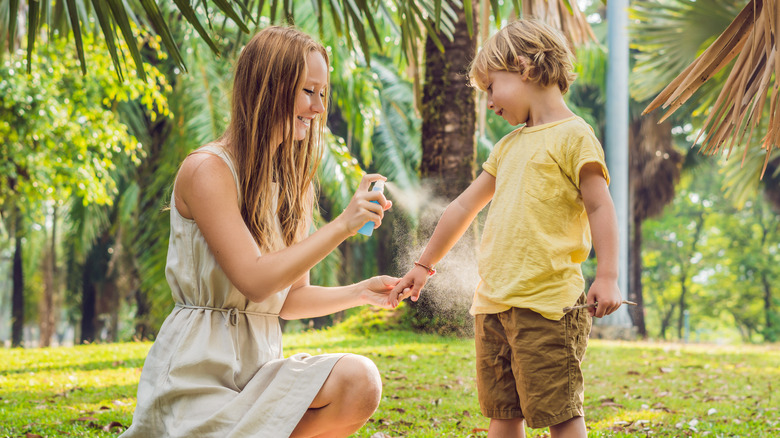 mom and son using insect repellant spraying on skin outdoors