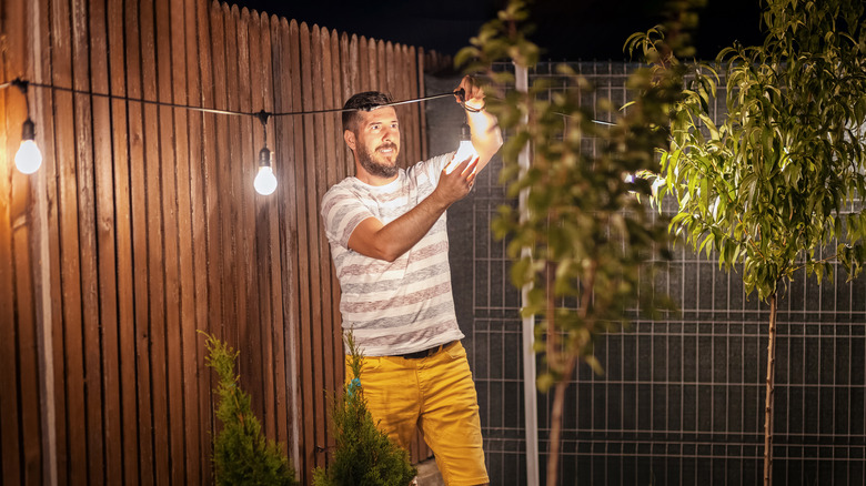 man setting up outdoor string lights decoration