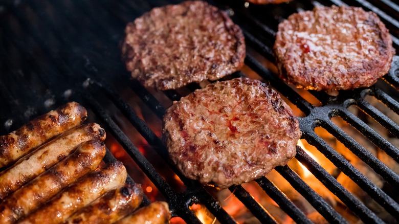 burgers and sausages on a grill on top of fire