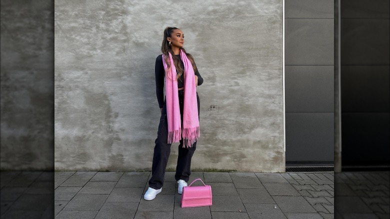 Woman in black outfit with pink scarf and purse