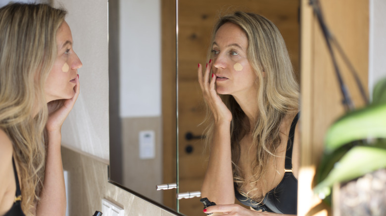 A middle-aged woman applying foundation in the mirror.