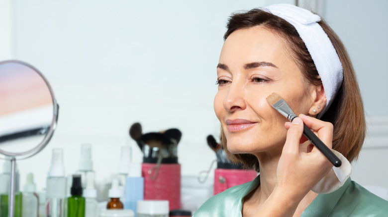 A midde-aged woman wearing a headband having her makeup done.