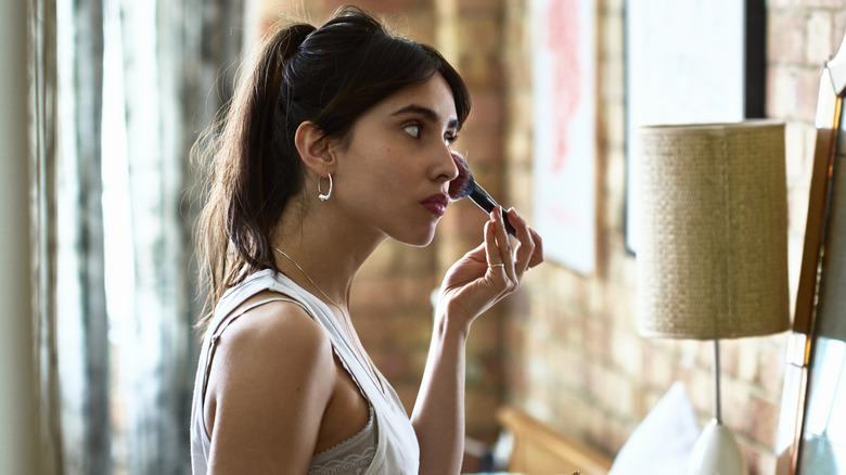 A woman with a ponytail applying blush.