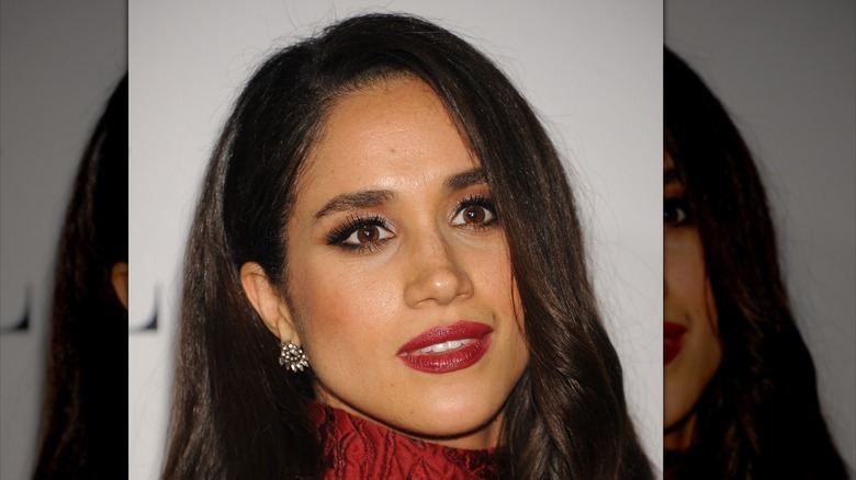 Meghan Markle posing with red lips and heavy eye makeup.