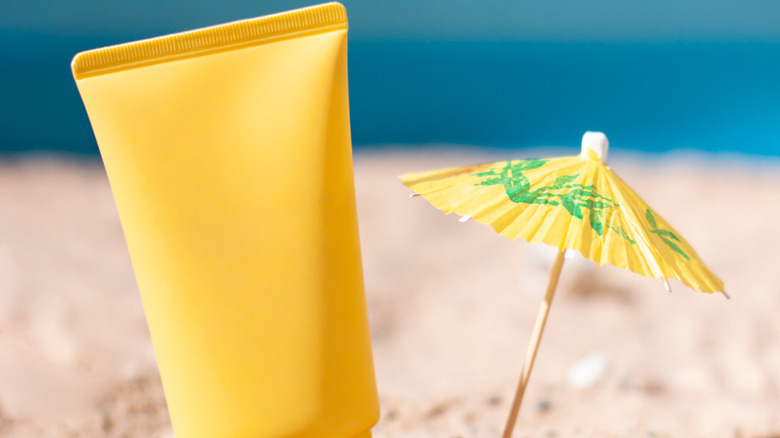 sunscreen bottle in the sand next to mini drink umbrella