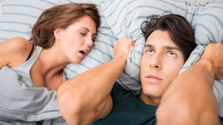 Man covering his ears while woman snores