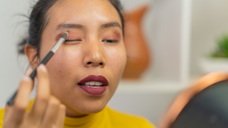 Woman in a yellow shirt applying eyeshadow