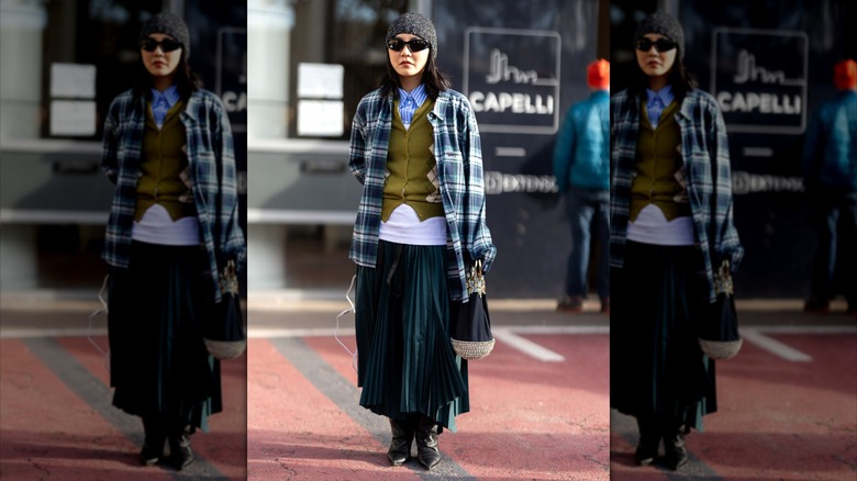 Woman with striped shirt, argyle sweater, plaid jacket, pleated maxi skirt