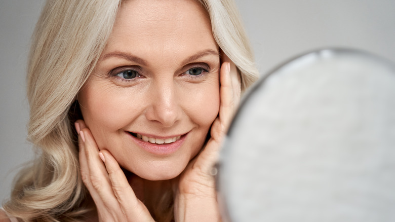 Middle aged woman looking into mirror and touching face