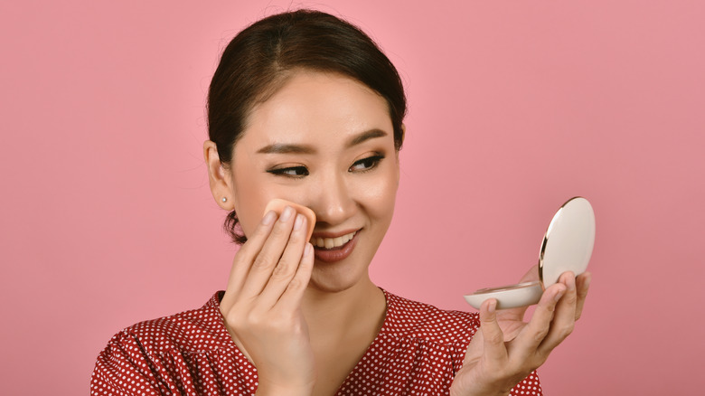 Young woman applying makeup with compact