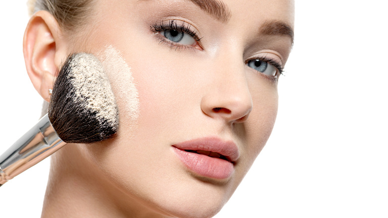 Young woman applying powder to face with brush